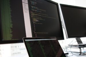 Developer working at a laptop with code displayed on dual monitors