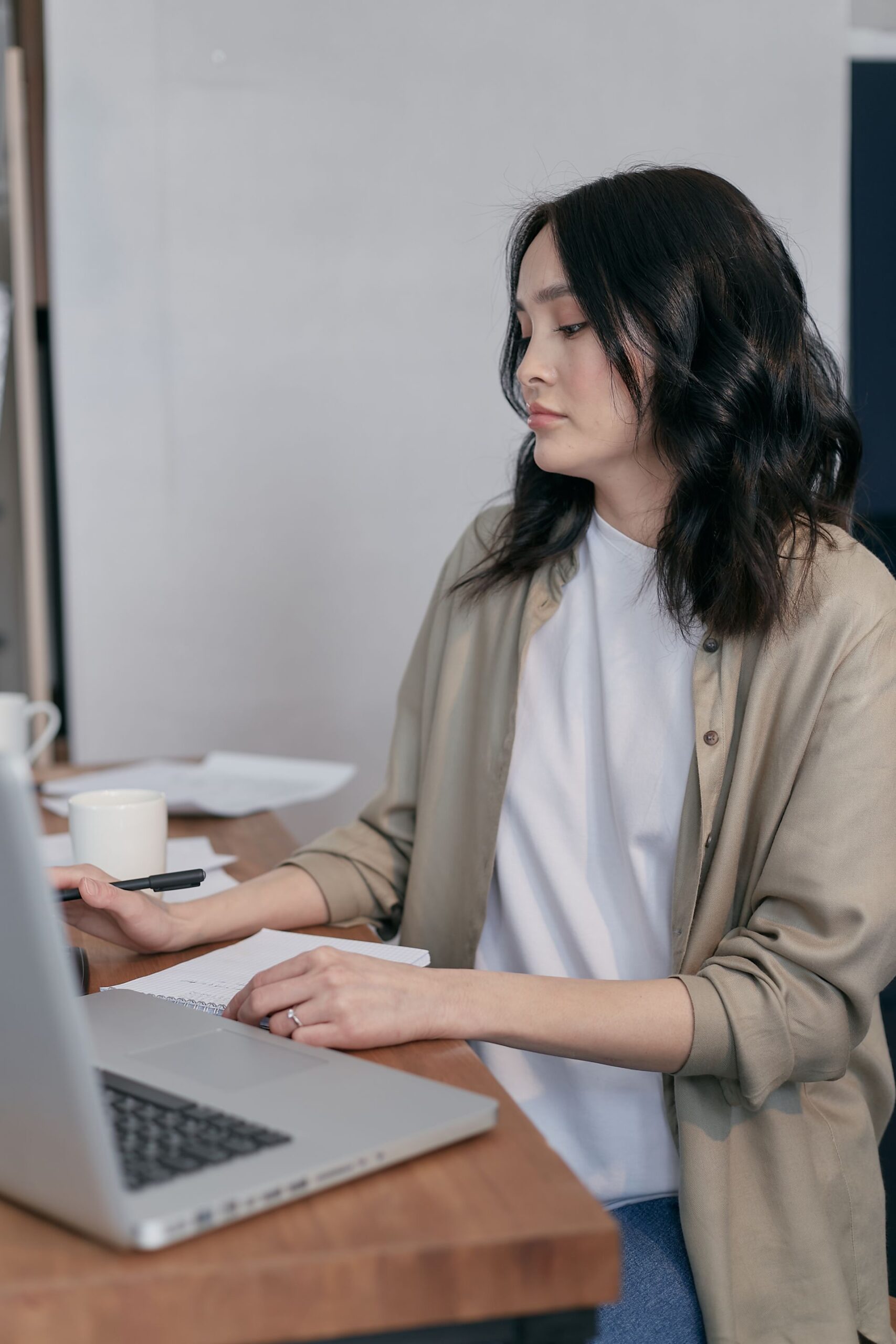 Woman writing in a notepad beside an open laptop